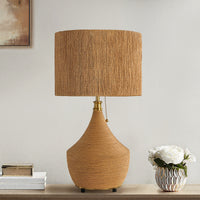 Natural rattan table lamp with woven drum shade styled on a table with white flowers
