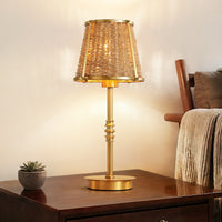 Gold rattan table lamp on a wooden bedside table beside a bed