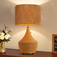 Lit boho rattan table lamp with woven paper rope shade on a wooden side table