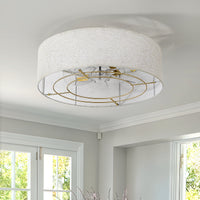 Gold flush mount ceiling fan with linen-blend shade installed in a bright interior
