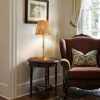 Gold rattan table lamp on a side table beside an upholstered armchair