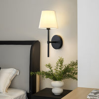Black linen shade wall sconce beside a bed